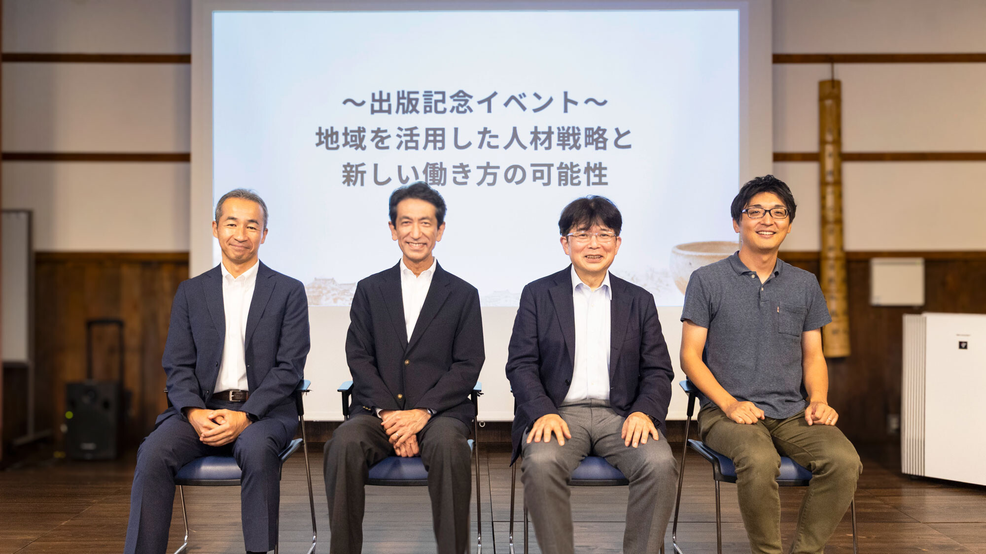 出版記念イベントのスクリーン前に並ぶ登壇者4名